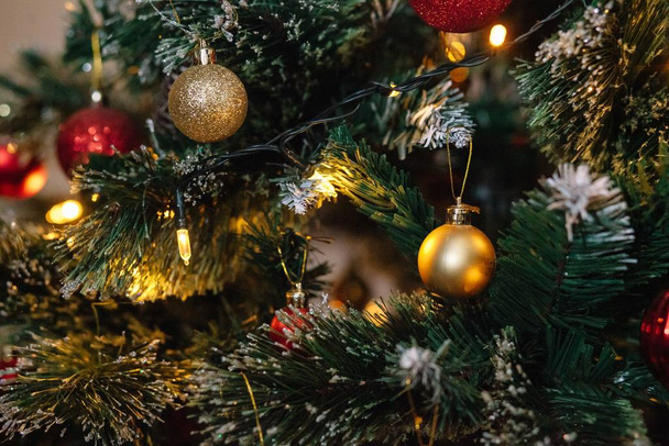 Red and golden balls on a Christmas tree with lights and bokeh. - Foto, afbeelding