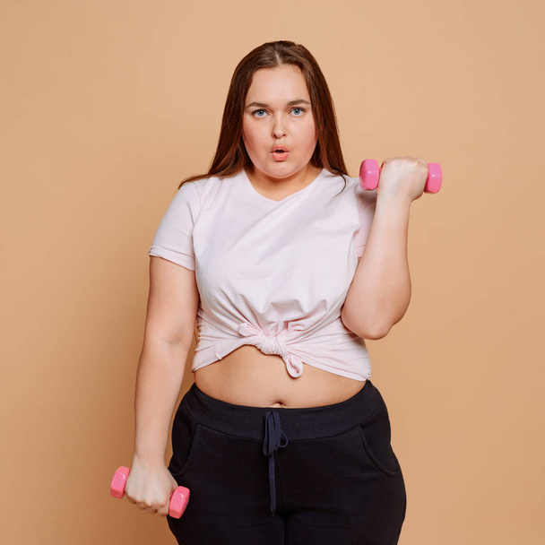 Woman doing alternate dumbbell curl exercise on beige background - Foto, afbeelding