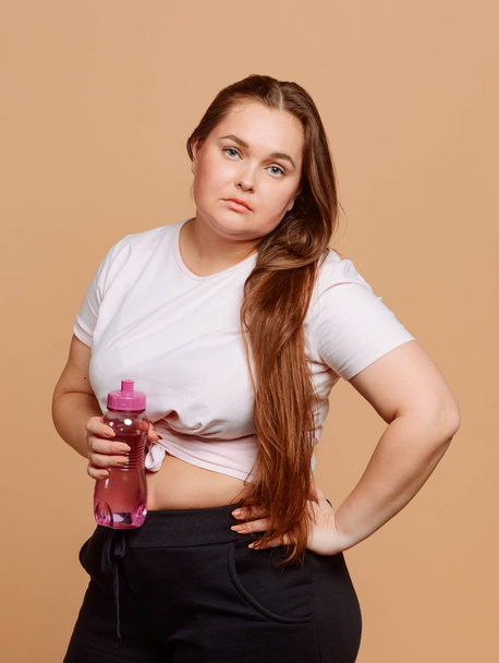 Bored girl with a bottle of water on beige background - Фото, изображение