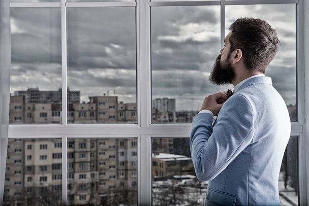 Life choices and expectations. Wedding day. Groom bearded hipster mature man wear light blue tuxedo and bow tie. Man stand at window nervous about wedding. Right decision. Wedding morning concept - Фото, зображення