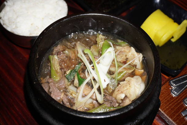 おいしいビビンバ韓国米と牛肉の卵黄身キノコゴマネギニンジン漬物混合調味料黒粘土鍋ボウルに伝統的な食品  - 写真・画像