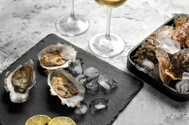 Piatto di ardesia con gustose ostriche fredde e vino su sfondo bianco
 - Foto, immagini