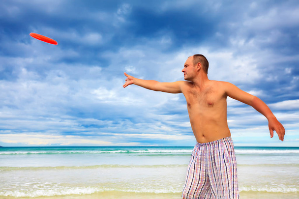 Young man is tossing a frisbee on the beach - Foto, imagen