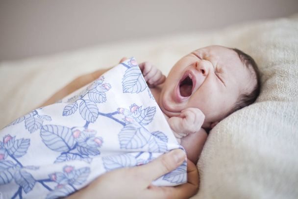 Portrait of a cute newborn baby girl lying wrapped in a blanket yawning - Zdjęcie, obraz
