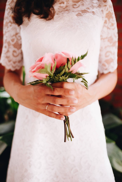 花嫁はピンクのバラの彼女の小さな結婚式の花束を保持。結婚式の日のコンセプト. - 写真・画像