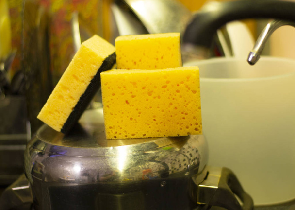 три жовті губки на кухні над сковородою біля раковини
 - Фото, зображення