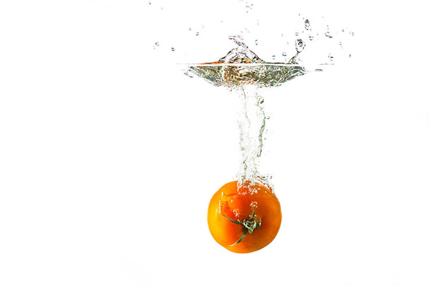 Tomaat die in het water valt met een plons geïsoleerd op witte achtergrond. - Foto, afbeelding