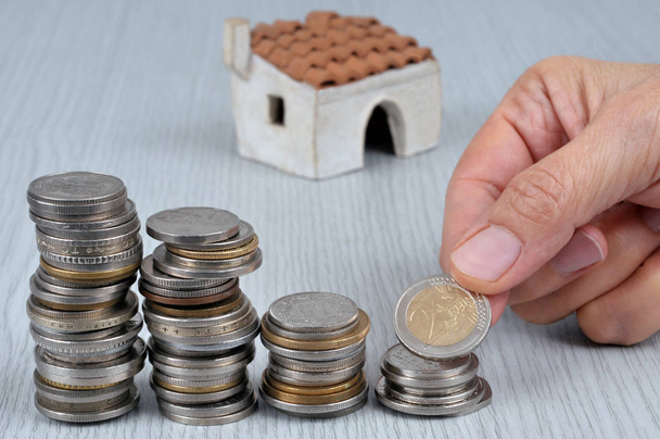 Hand stapelt Münzen mit einem Haus im Hintergrund - Foto, Bild