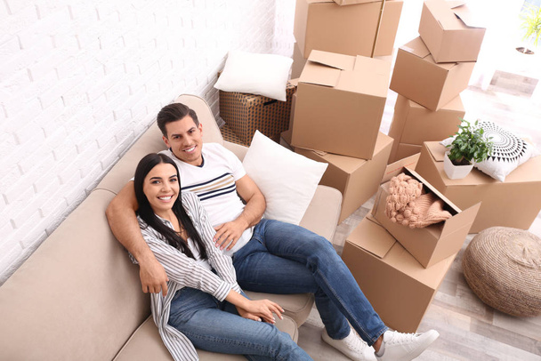 Happy couple resting in room with cardboard boxes on moving day, - Foto, Bild