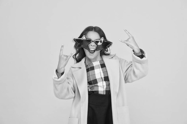 She goes crazy. Crazy child show horns sign hand gesture. Happy girl with crazy look yellow background. Fashion kid wear star shaped glasses. Crazy holiday mood. School holidays - Фото, изображение