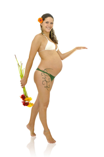 Pregnant woman with tattoo in bikini holding a bunch of flowers isolated in white - Фото, изображение