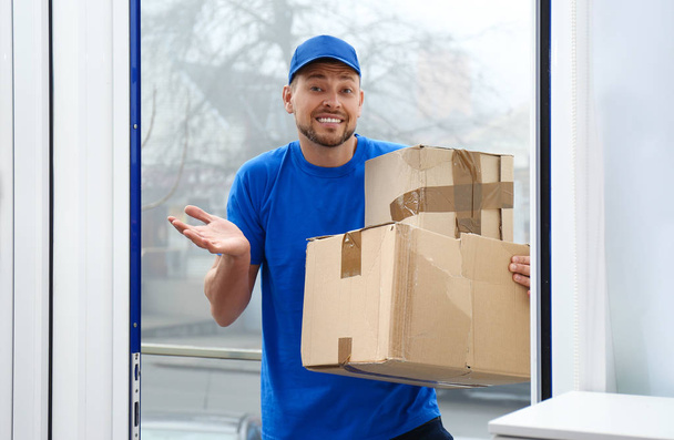 Emotional courier with damaged cardboard boxes in doorway. Poor  - Φωτογραφία, εικόνα