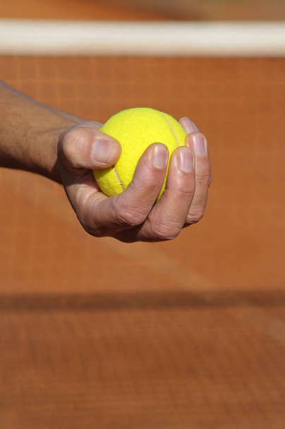 Closeup of a hand with a tennis ball in a clay court - Фото, изображение