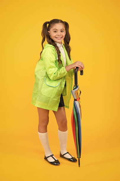 Fashionable and comfortable. Happy schoolchild with fashionable autumn look on yellow background. Small girl smiling in fashionable raincoat with umbrella cane. Having fun with fashionable colors - Photo, Image