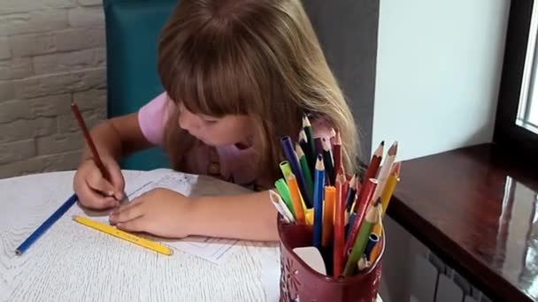 mała dziewczynka siedzi w pobliżu okna i rysuje - Materiał filmowy, wideo