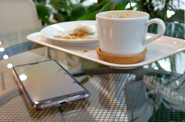 Ontbijt in het café. Op tafel vuile vaat - een koffiebeker en een bord - en een smartphone. - Foto, afbeelding