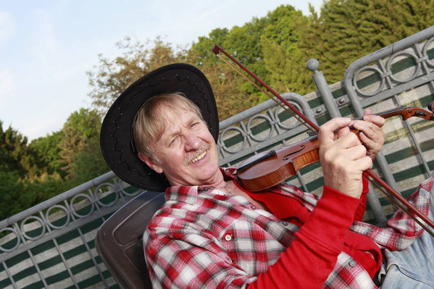 mature man plays the violin on a balcony - Foto, Imagen