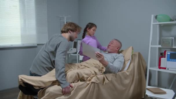 Boy and girl talk to their grandfather who lying on bed  - Video, Çekim