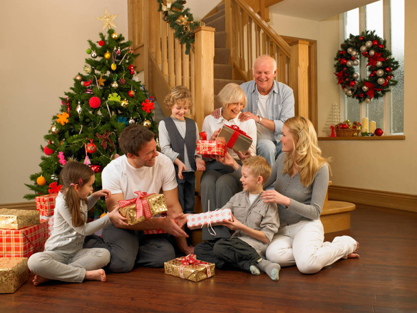 A család ajándékot cserél a karácsonyfa előtt. - Fotó, kép