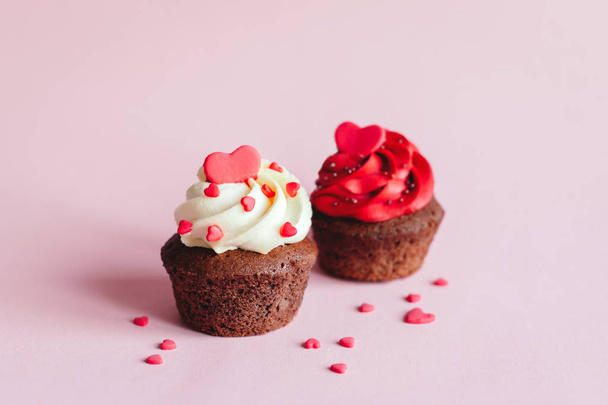 ピンクのパステルを背景に甘い心で装飾されたバレンタインカップケーキ.  - 写真・画像