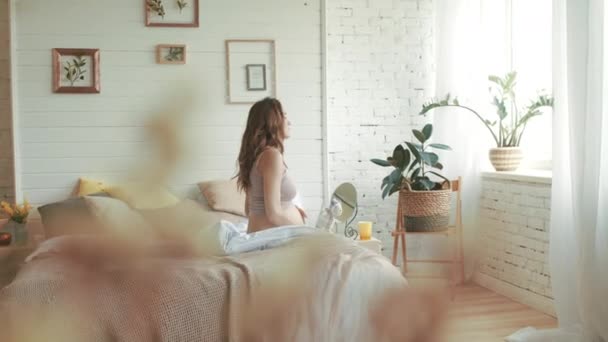 Pregnant woman getting up in bedroom. Expectant mother stroking belly at home - Filmagem, Vídeo