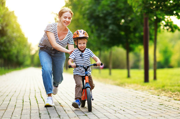 gelukkige familie moeder leert kind zoon om een fiets in het park te rijden - Foto, afbeelding