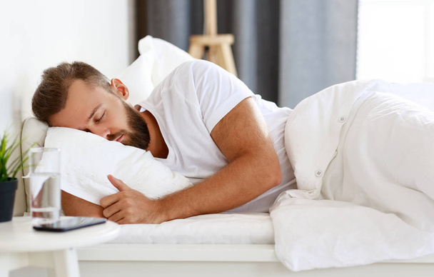 young man sleeping in bed in bedroom in mornin - Фото, изображение