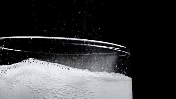 Glass with hissing carbonated bubbles. Stock footage. Close-up of carbonated foam bubbling and sizzling formed to edge of glass on black isolated background - Footage, Video