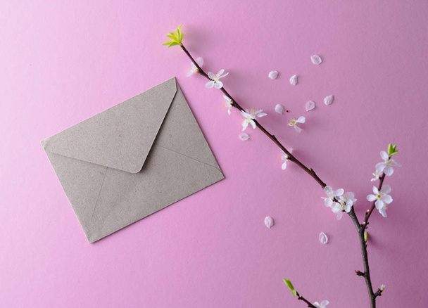 Beiger Umschlag zum Schreiben und ein blühender Aprikosenzweig auf rosa Hintergrund. Einladung zur Party - Foto, Bild