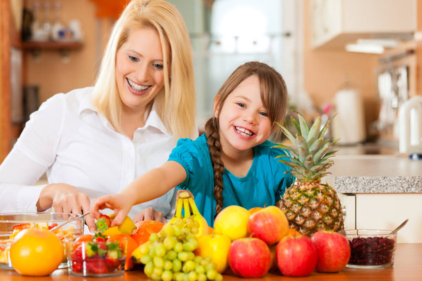 healthy eating - mother and child sitting in the kitchen with different kinds of fruit - Фото, изображение