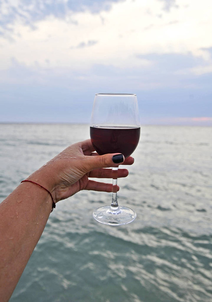 Verres à vin avec vin rouge à la main féminine sur la plage du coucher du soleil
.  - Photo, image