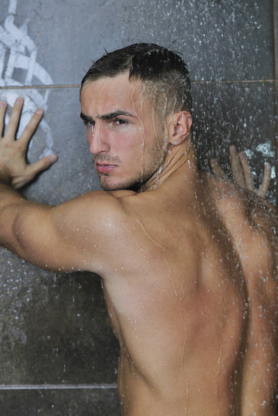 young good looking and attractive man with muscular body wet taking showe in bath with black tiles in background - Foto, imagen