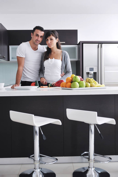 幸せな若いカップルは、モダンなキッチンの新鮮な果物や野菜のサラダを準備している間屋内で楽しい時を過す - 写真・画像