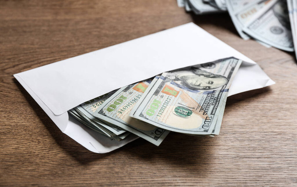 Umschlag mit Dollarscheinen auf Holztisch. Schmiergeld-Konzept - Foto, Bild