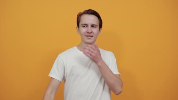 Hombre feliz en blanco t-corto se ríe y señala el dedo a un lado en un amarillo
 - Metraje, vídeo