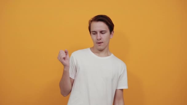 Νεαρός άνδρας με λευκό t πουκάμισο σε κίτρινο φόντο κοιτάζει με σιγουριά προς τα εμπρός - Πλάνα, βίντεο