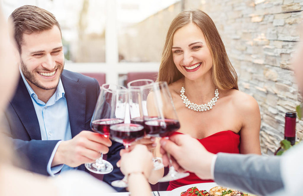 Les gens assis sur la table du restaurant grillent avec du vin rouge
 - Photo, image