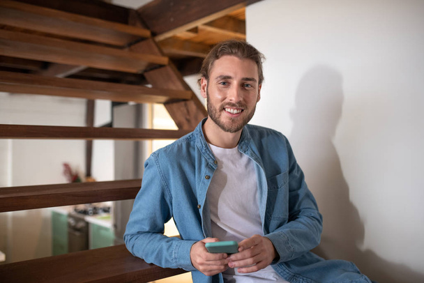 Smiling young man holding his smartphone in hands - Photo, image
