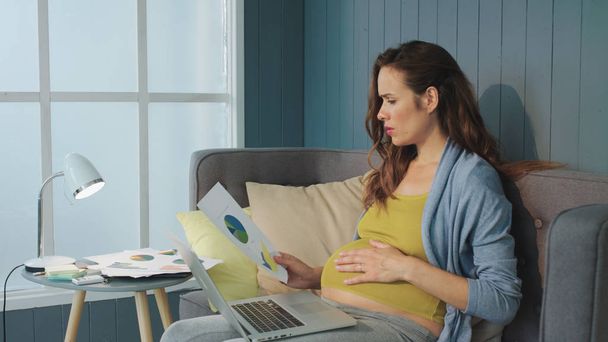 Zwangere vrouw die zakelijke diagrammen analyseert. Buik moeder op het werk - Foto, afbeelding
