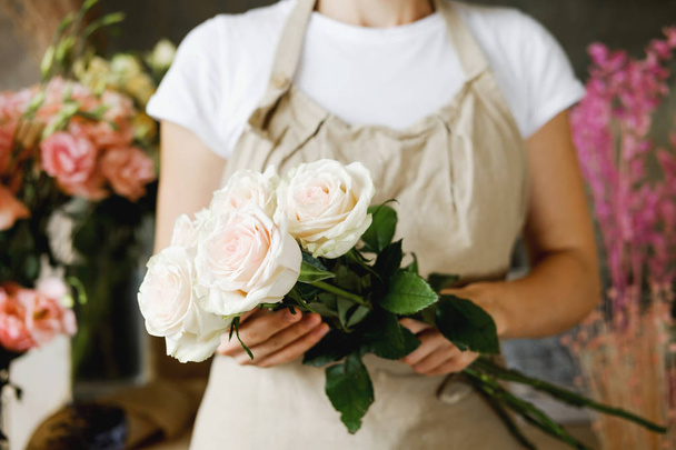 ανθοπωλείο γυναίκα στέκεται με μπουκέτο από ροζ τριαντάφυλλα σε εσωτερικούς χώρους στο ανθοπωλείο. Επιχειρηματικότητα, μικρές επιχειρήσεις, έννοια του χώρου εργασίας - Φωτογραφία, εικόνα