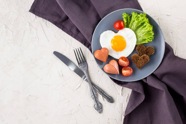 Ημέρα του Αγίου Βαλεντίνου πρωινό με τηγανητά αυγά σε σχήμα καρδιάς σερβίρεται σε γκρι πιάτο. - Φωτογραφία, εικόνα
