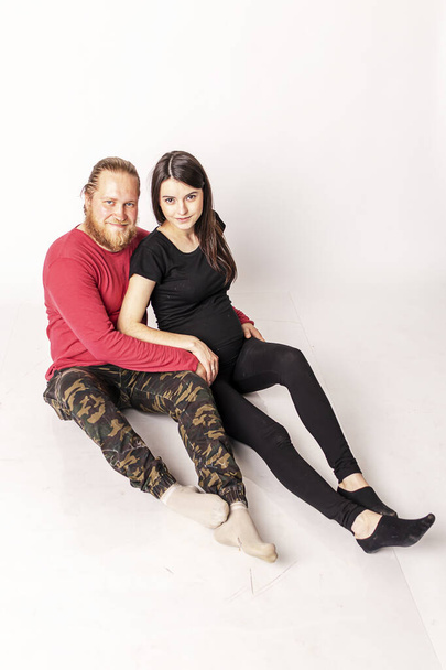 Caucasian man with a beard in a red sweater hugs a pregnant Caucasian girl - Fotografie, Obrázek