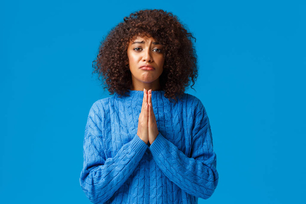 Prosím, pomozte mi. Trucující pochmurný roztomilý africko-americká přítelkyně s afro sestřihem, tisknout ruce k sobě v modlitbě, prosit, prosit omluvu, omlouvám se za omyl, žebrání přes modré pozadí - Fotografie, Obrázek
