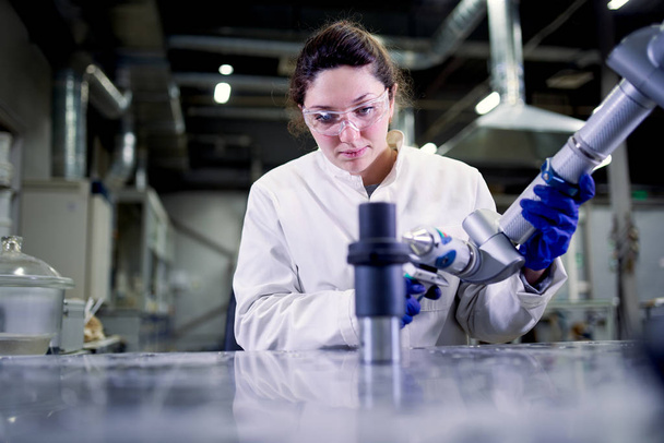 Female lab technician in blue rubber gloves with 3D printer on blurred background - Foto, imagen