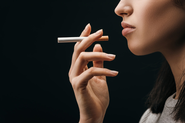 Πλευρική άποψη της γυναίκας που κρατά το τσιγάρο απομονωμένο σε μαύρο  - Φωτογραφία, εικόνα