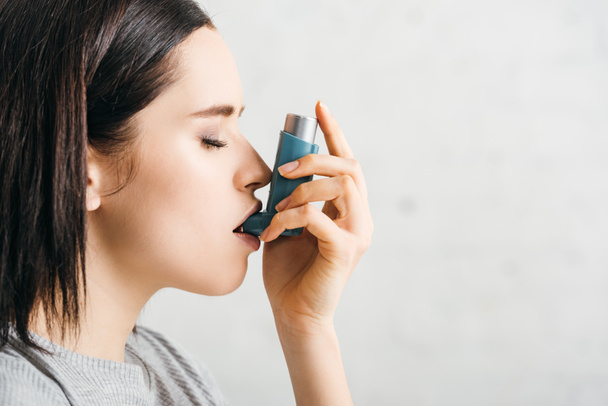 Vista lateral de chica atractiva usando inhalador asmático sobre fondo blanco
 - Foto, imagen