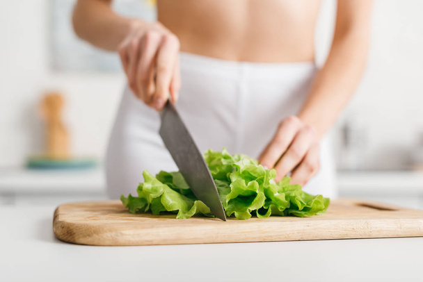 Selective focus of slim woman cutting fresh lettuce on kitchen table - Фото, изображение
