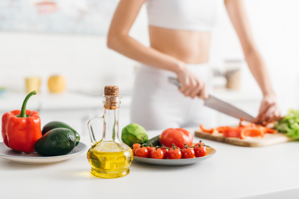 Foco seletivo de legumes orgânicos e abacate perto de esportista salada de cozinha na mesa da cozinha
 - Foto, Imagem