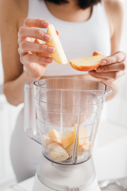 Cropped view of young sportswoman putting fruits in blender on kitchen table - Photo, Image