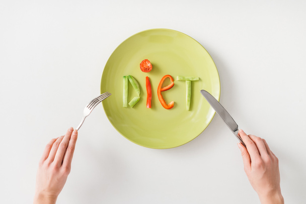Κάτοψη της γυναίκας με μαχαιροπήρουνα κοντά λέξη δίαιτα από φέτες λαχανικών στο πιάτο σε λευκό φόντο - Φωτογραφία, εικόνα